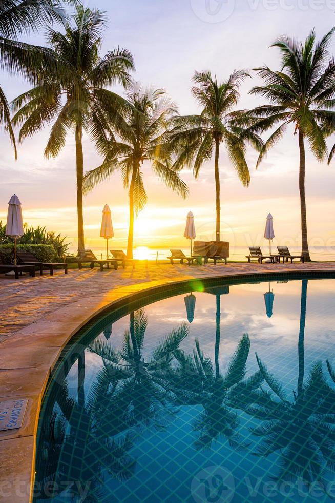 guarda-chuva e cadeira ao redor da piscina em hotel resort com nascer do sol pela manhã foto