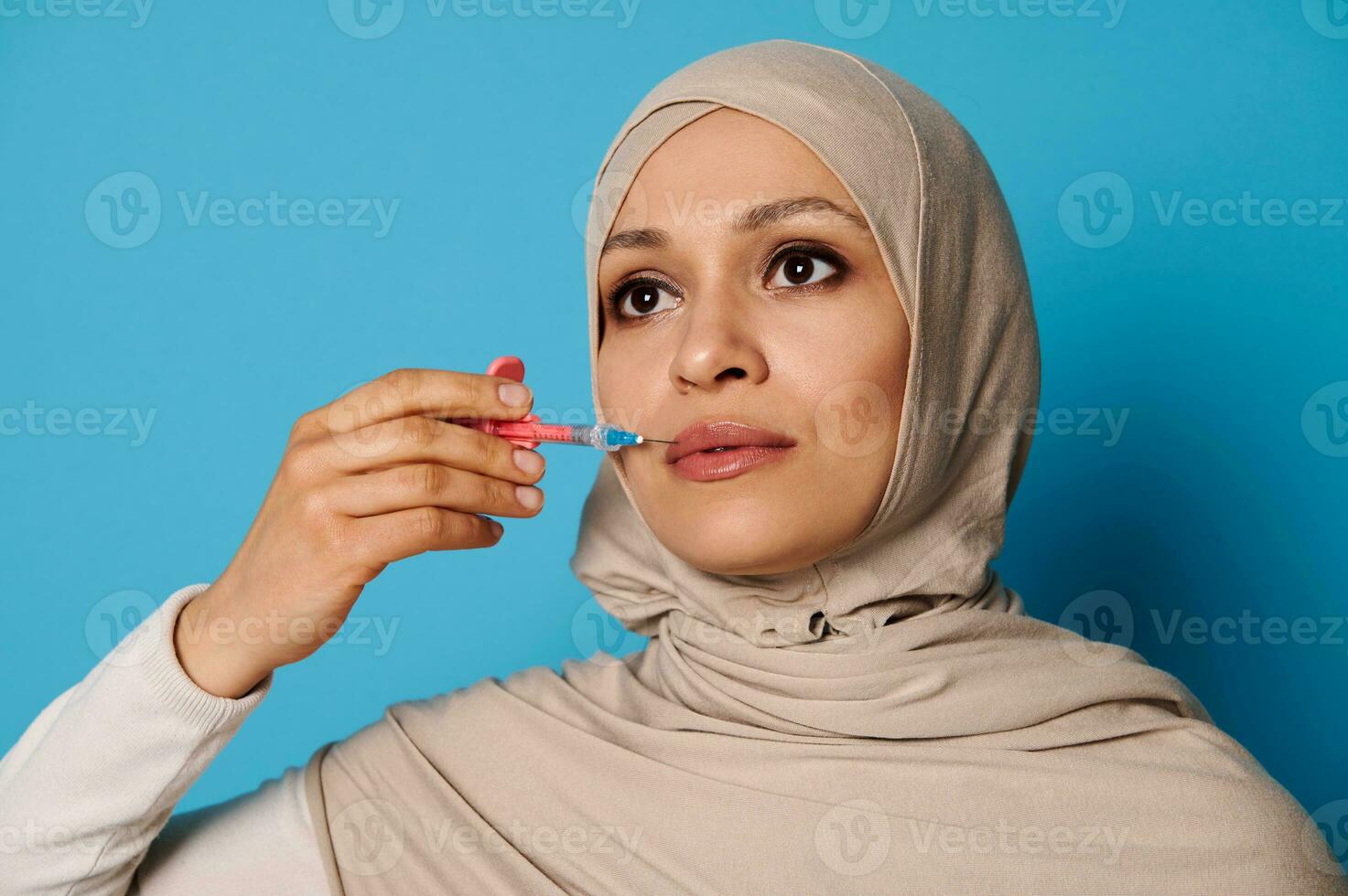 fechar-se do lindo muçulmano mulher dentro hijab segurando uma seringa com beleza injeção perto dela lábios. lábios aumento conceito dentro injeção cosmetologia foto