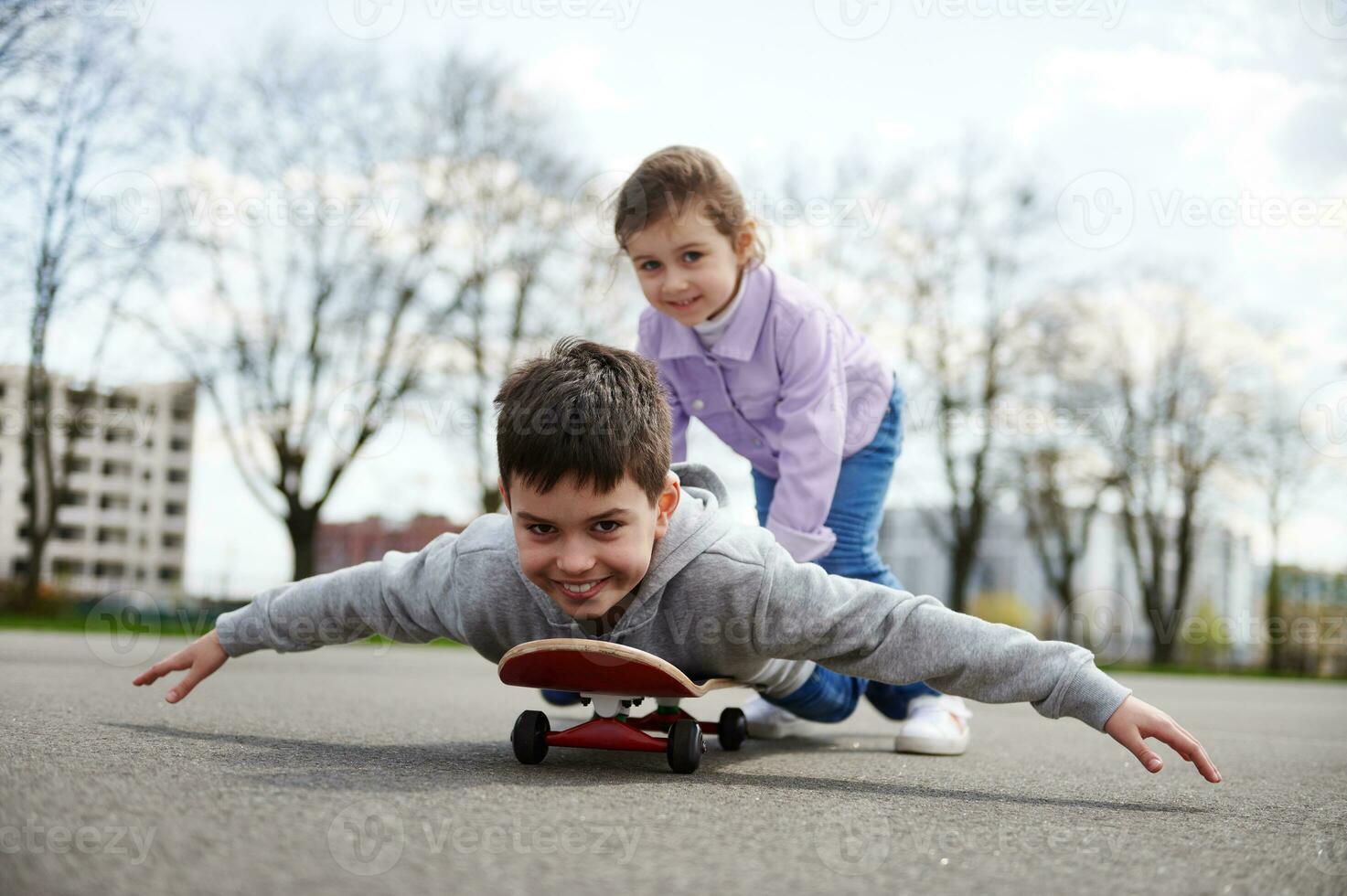 sorridente menina equitação dela irmão em uma de madeira skate desfrutando uma jogos juntos em uma Esportes terra foto