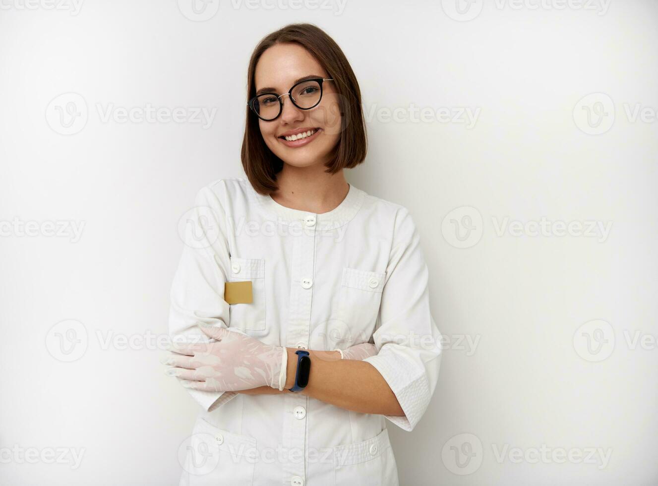 sorridente jovem fêmea médico estagiário posando com cruzado braços contra branco fundo com cópia de espaço foto