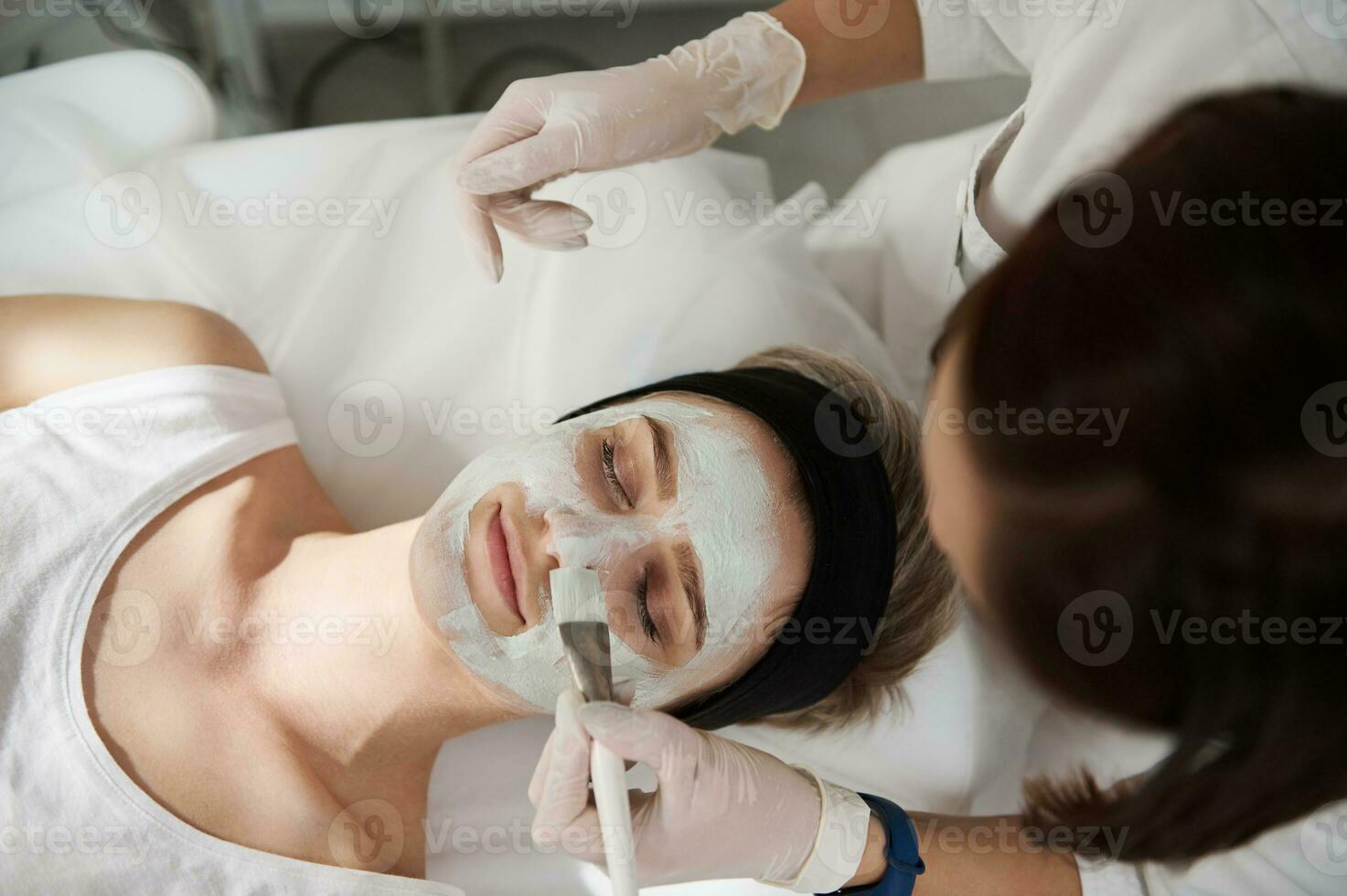 Alto ângulo Visão do uma mulher recebendo Cosmético procedimento dentro spa Centro. hidratante face mascarar . facial pele tratamento. foto