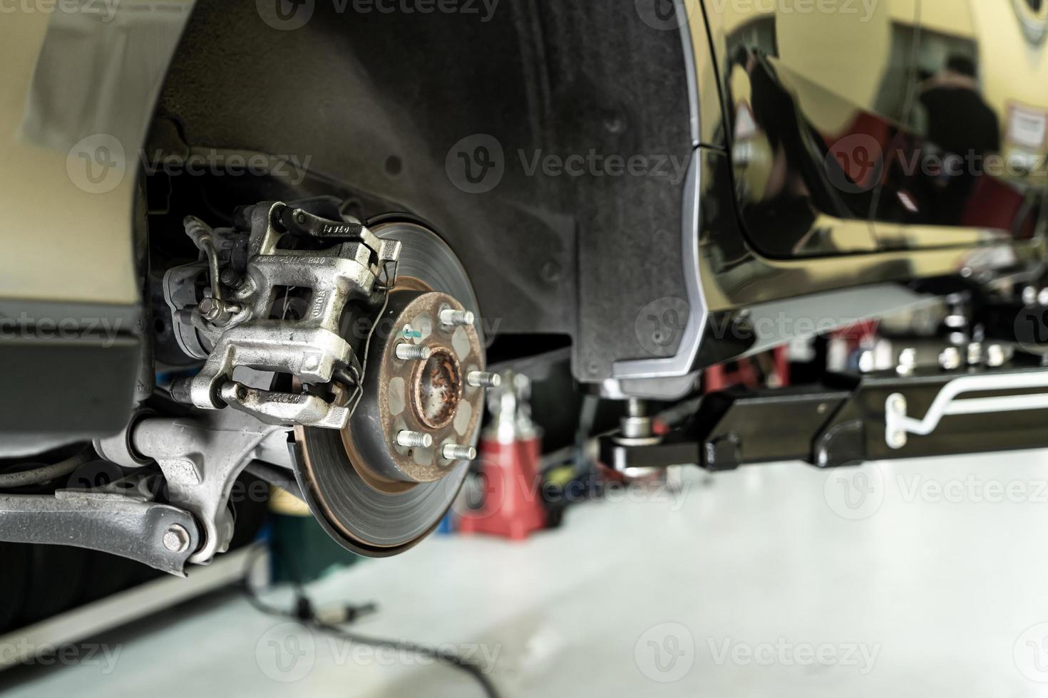 close up do carro do disco - mecânico desparafusando as peças do automóvel enquanto trabalhava sob um carro levantado foto