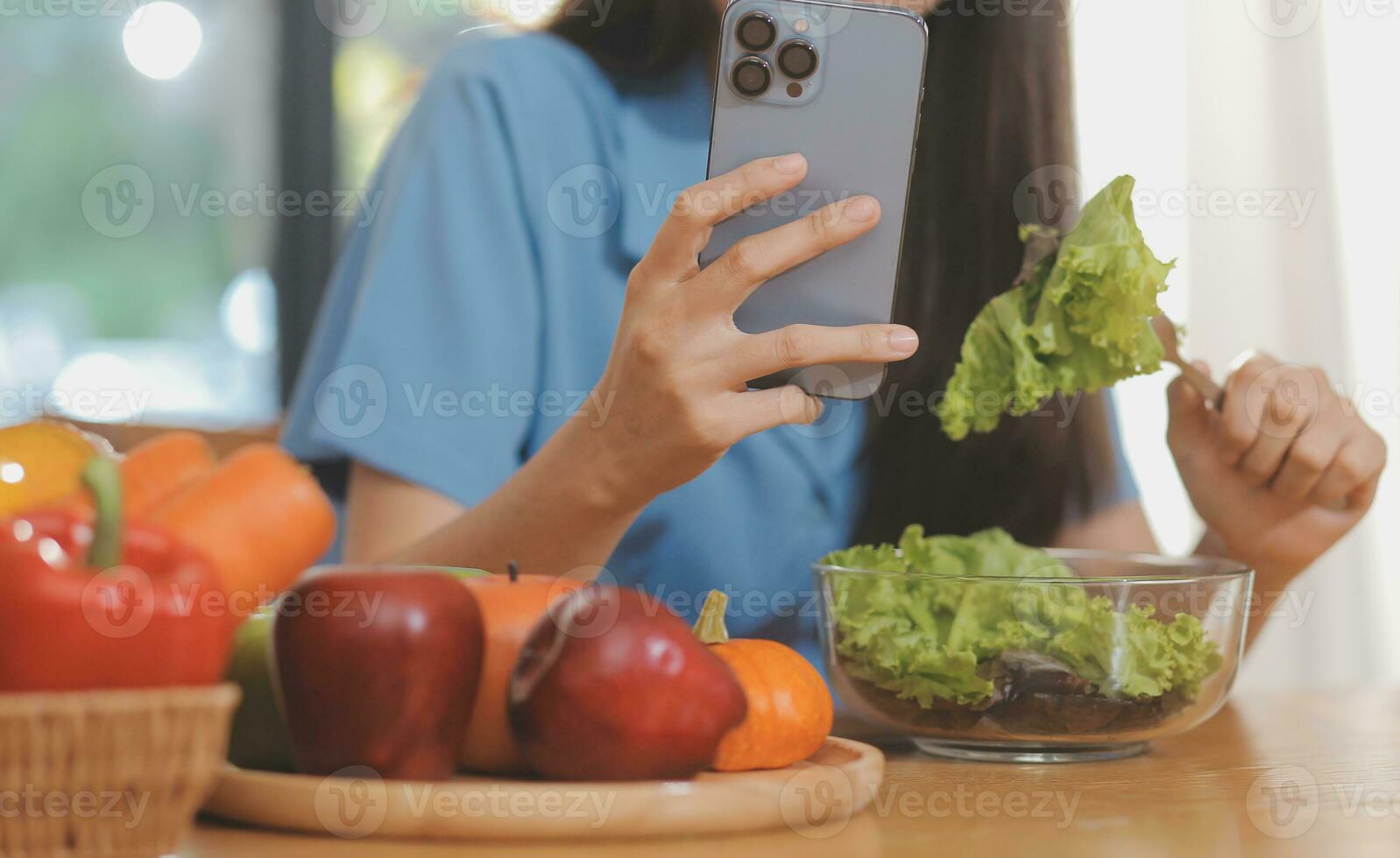 uma jovem mulher com uma lindo face dentro uma azul camisa com grandes cabelo comendo fruta sentado dentro a cozinha às casa com uma computador portátil e caderno para relaxamento, conceito período de férias. foto