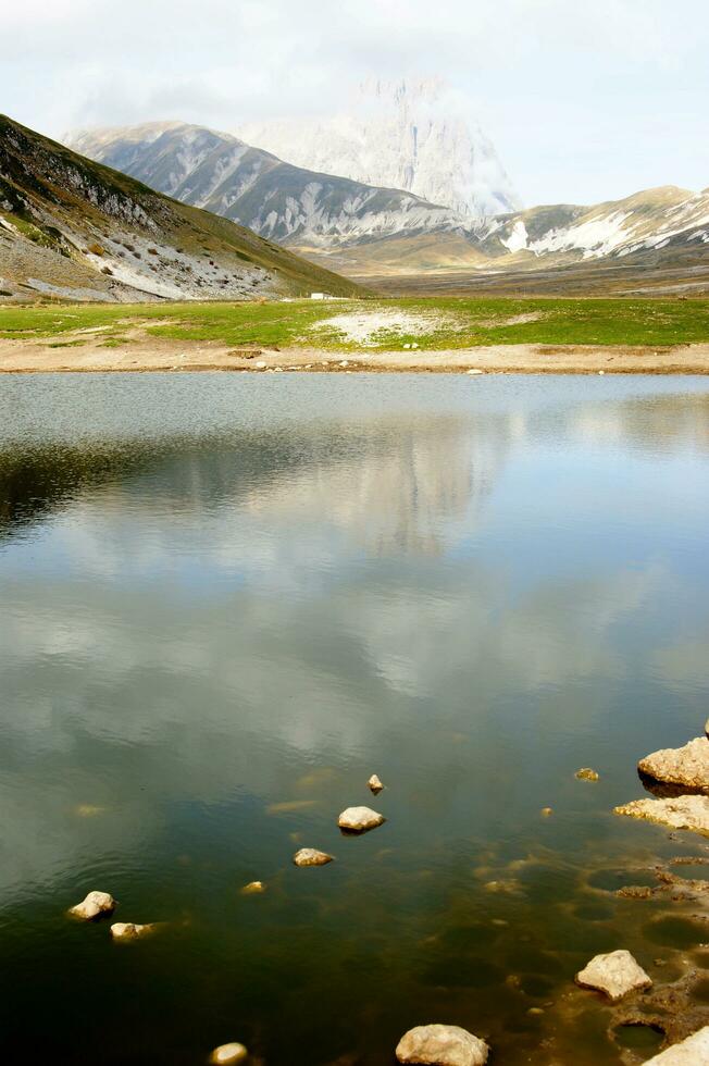 uma pessoa sentado em uma Rocha perto uma lago foto