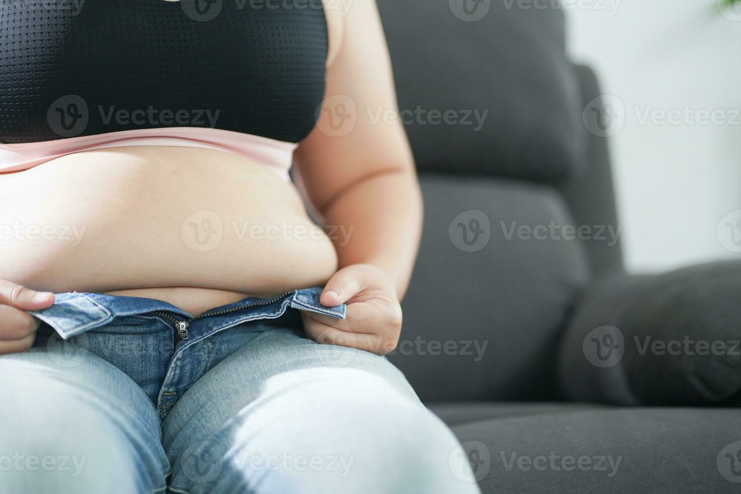 obeso mulher com gordo chateado sobre dela barriga. excesso de peso mulher tocante dele gordo barriga e quer para perder peso. gordo mulher com justa roupas preocupado sobre peso dieta estilo de vida conceito foto