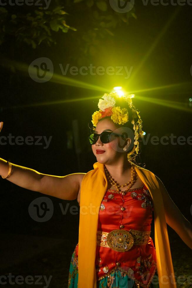 uma lindo sundanês dançarino poses e danças dentro uma glamouroso vestir e cachecol dentro frente do a etapa luz foto