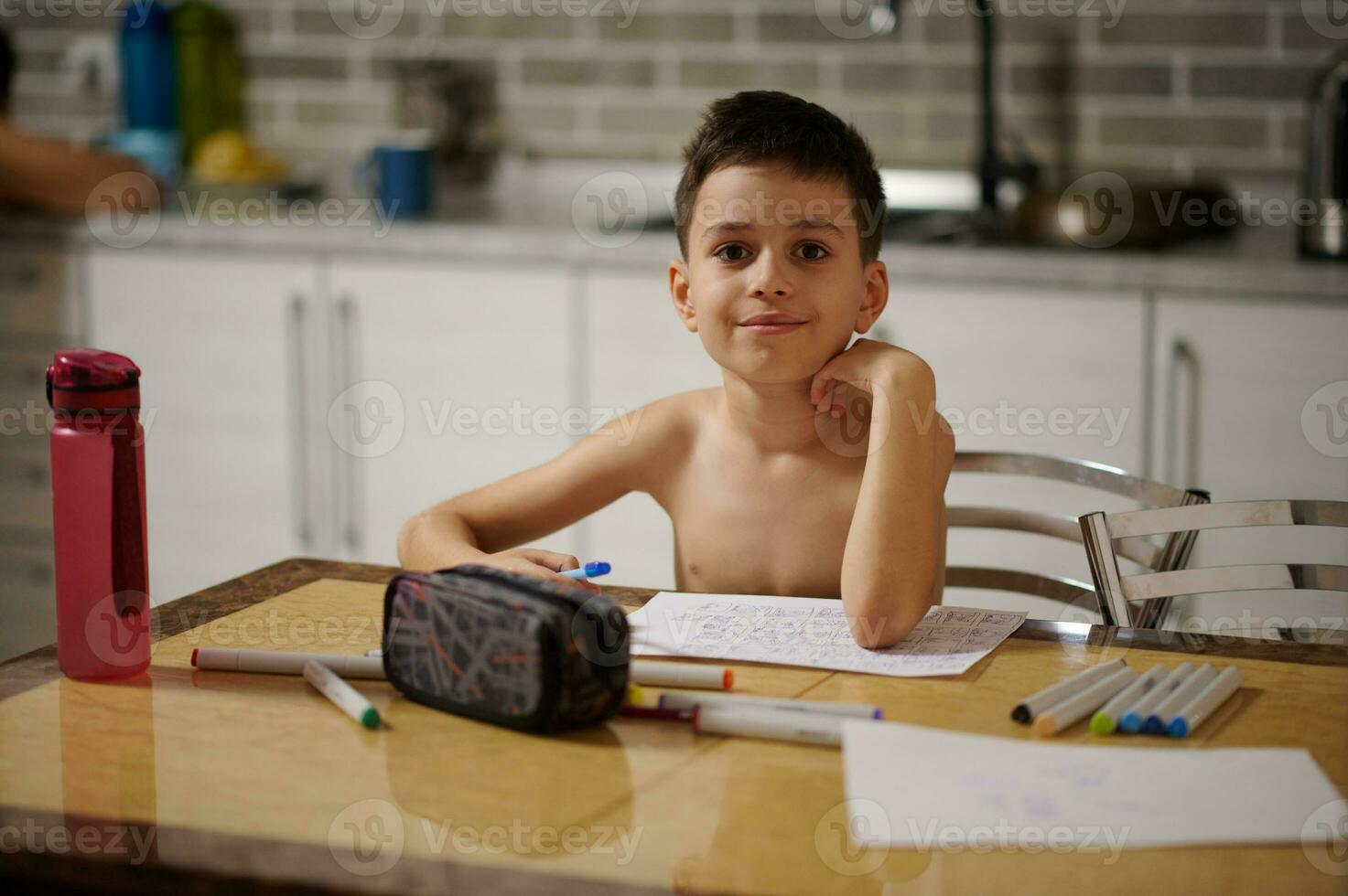 adorável Garoto olhando às a Câmera enquanto sentado às a mesa e desenhando As fotos às casa