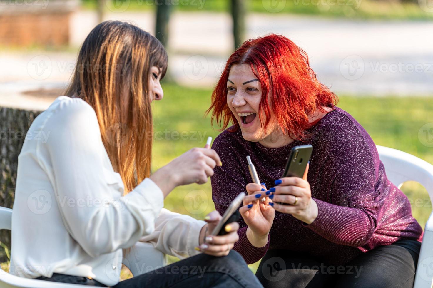 amigas usando smartphone e fumando cigarro foto