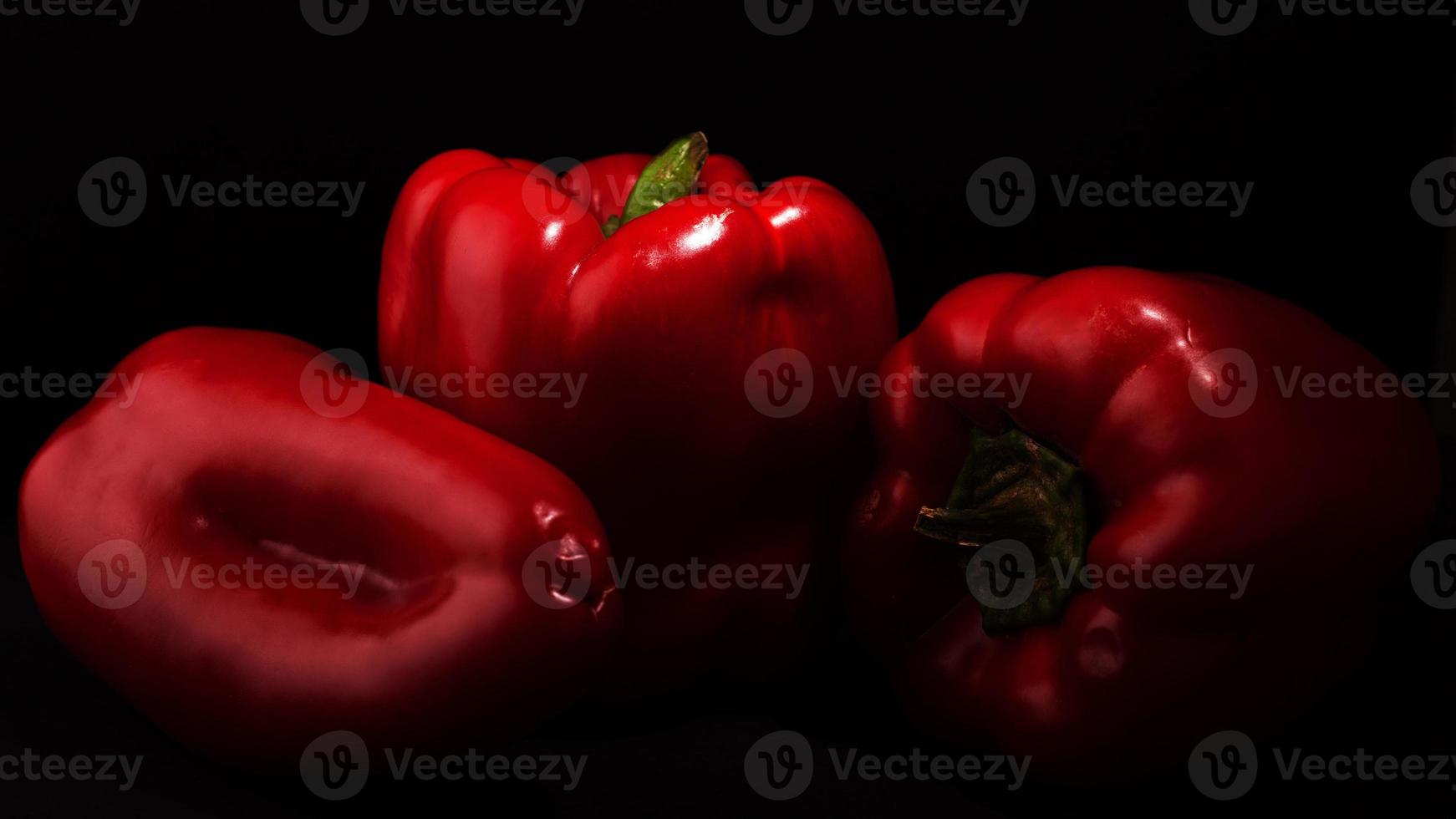 três pimentas vermelhas doces com colorau em fundo preto foto
