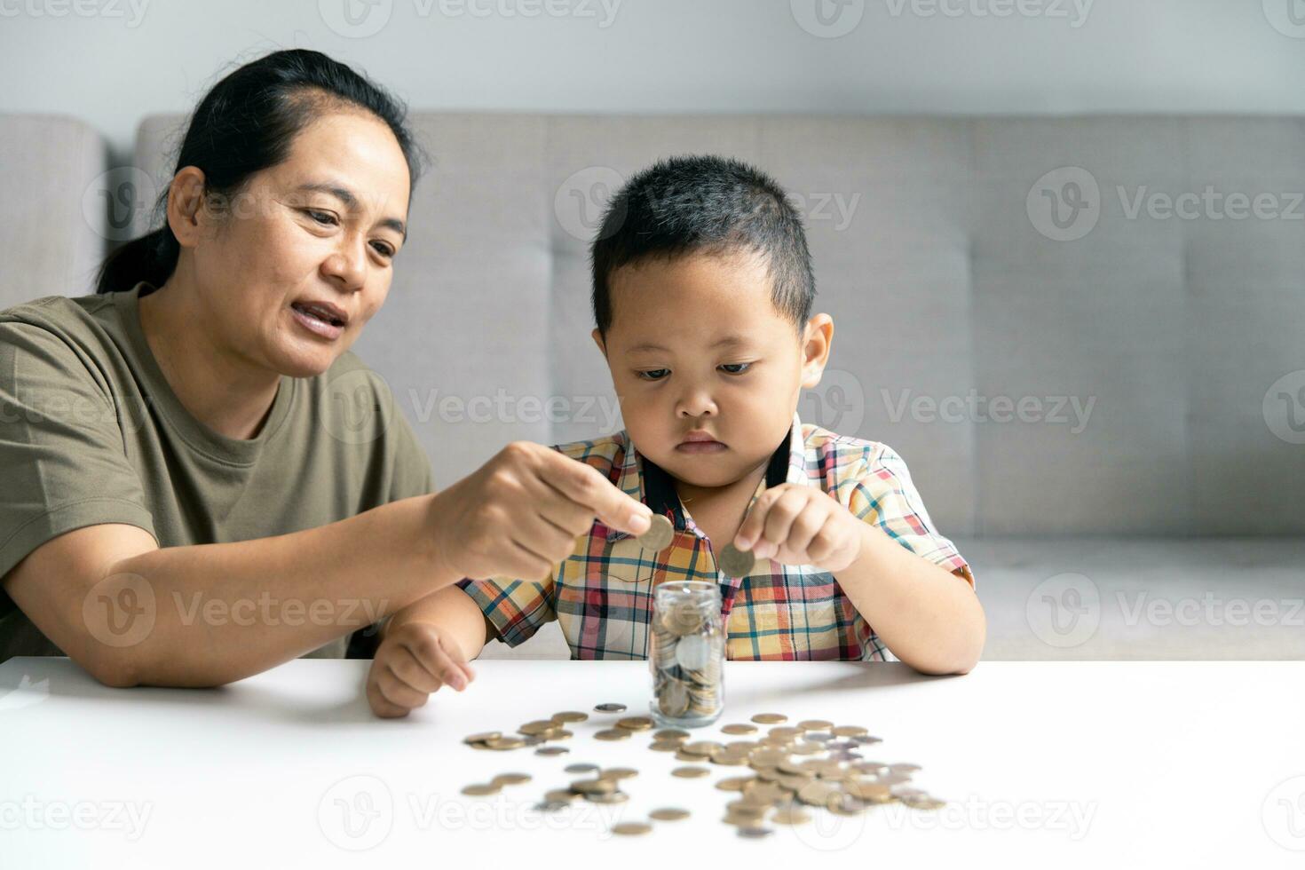 feliz ásia criança e mãe salvando dinheiro junto, colocando dinheiro para dentro porquinho banco. mãe jogando com criança em aquecimento chão às lar, ensino pequeno filho para investir dinheiro, planejamento futuro. foto