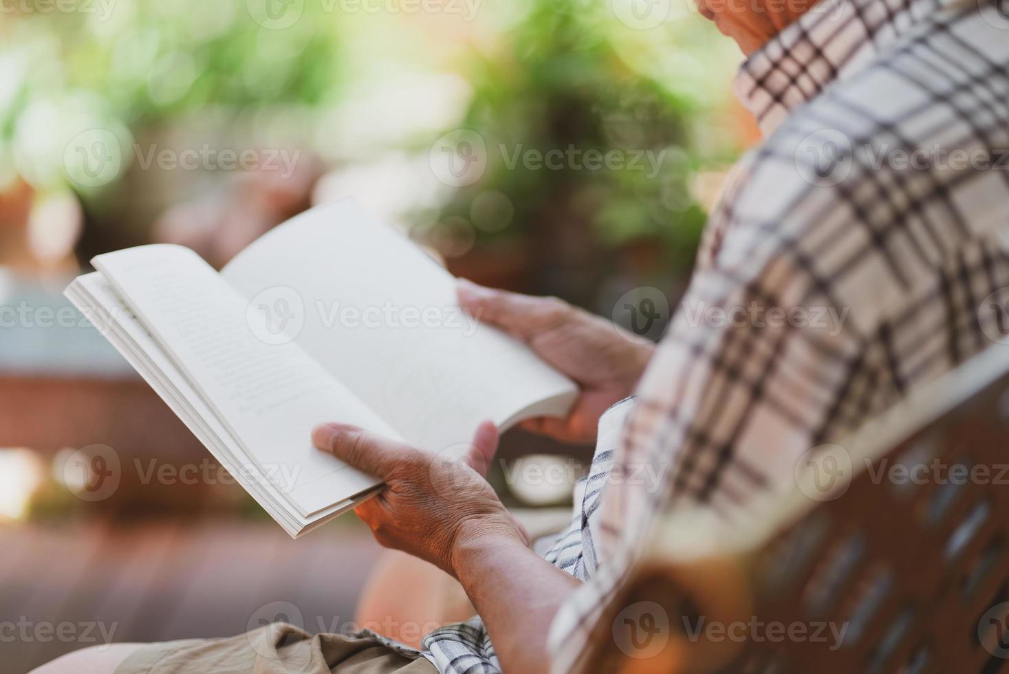 idoso asiático aposentado sentado no banco e lendo um livro no quintal de casa durante o tempo livre foto