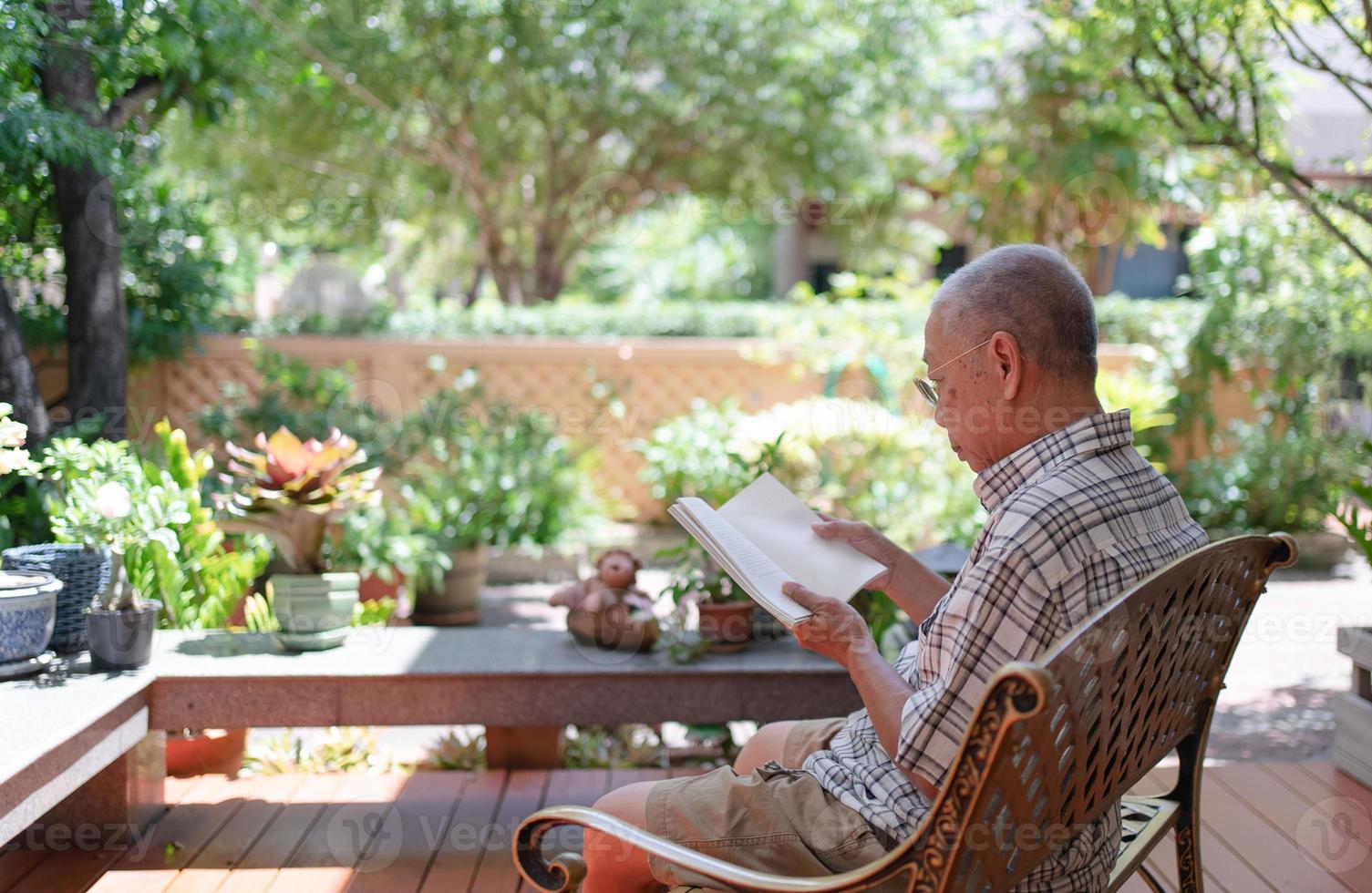 idoso asiático aposentado sentado no banco e lendo um livro no quintal de casa durante o tempo livre foto