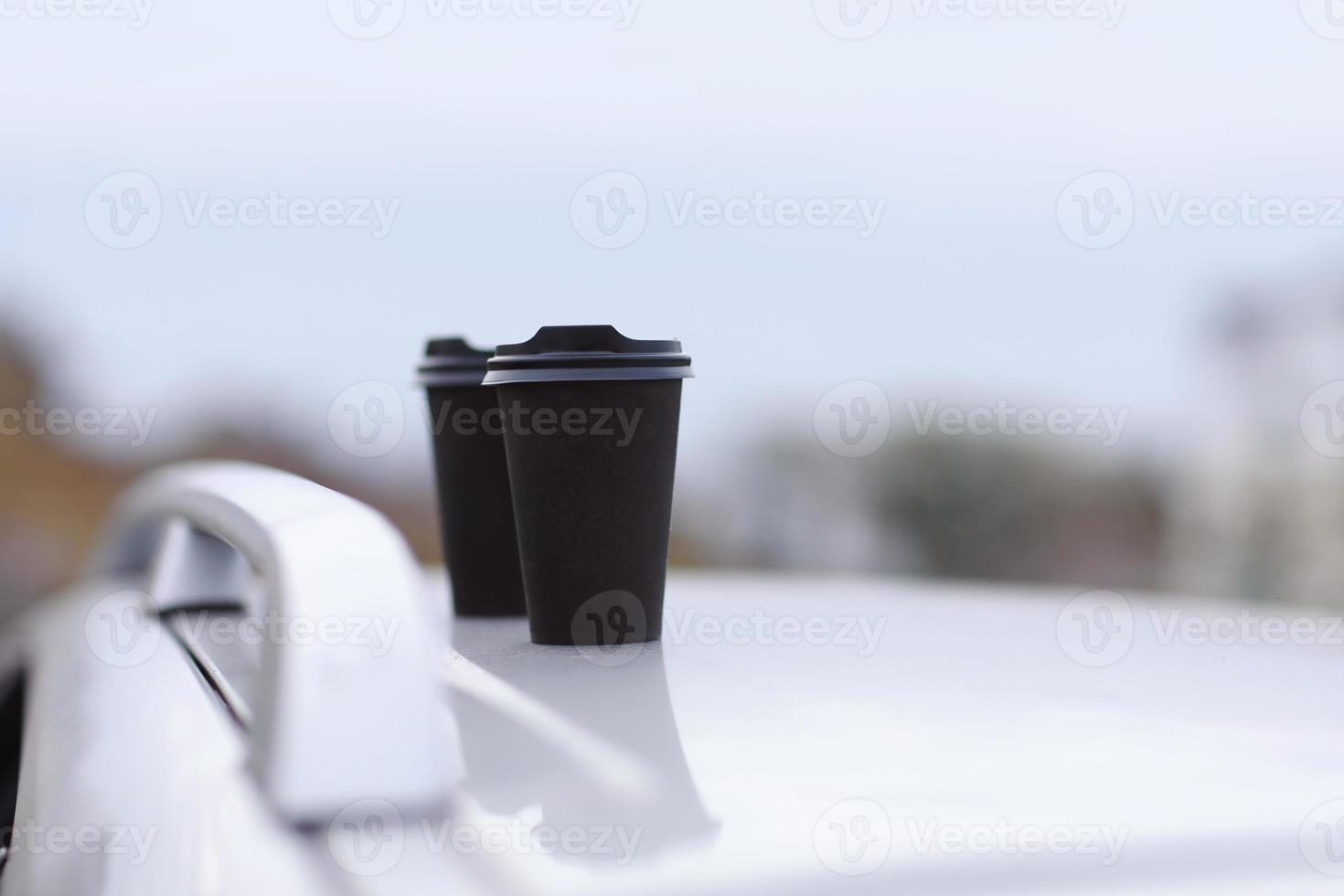 dois copos pretos de bebidas em um carrinho em um fundo desfocado da cidade. café ou chá para viagem em copos descartáveis. um lanche rápido. xícaras de café no carro. foco seletivo foto