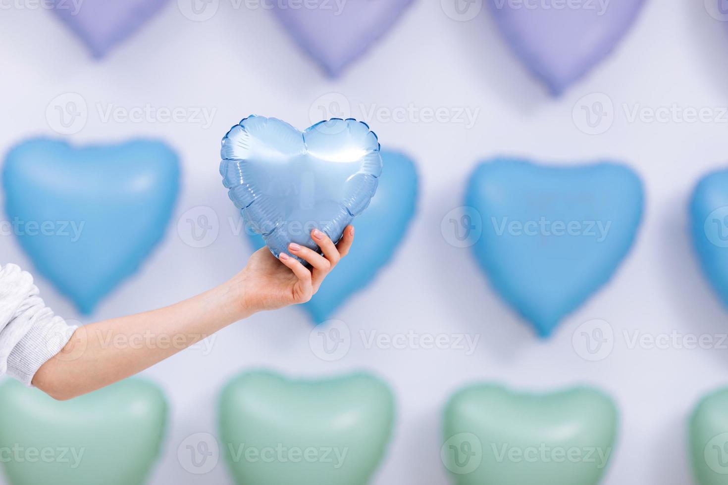 a mulher segura o balão azul na forma de um coração no fundo de muitos corações. Dia dos Namorados. foco seletivo foto