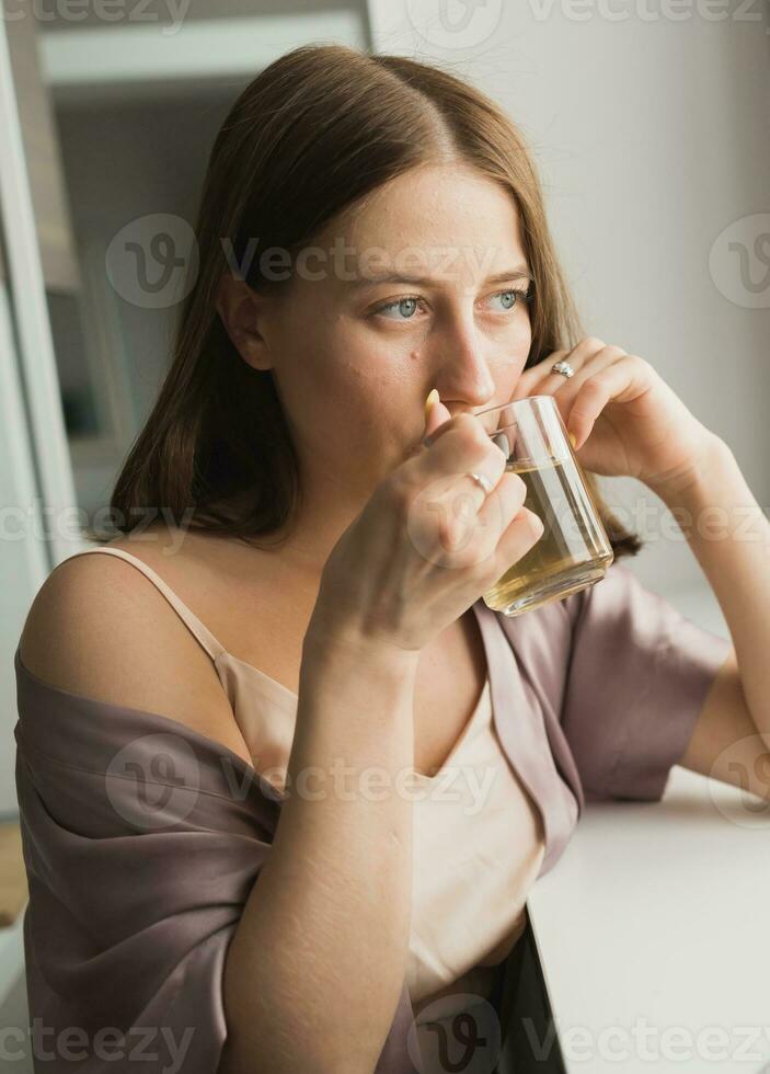 jovem mulher sentado em cadeira às casa e bebendo chá, casual estilo interior atirar. fechar-se retrato foto