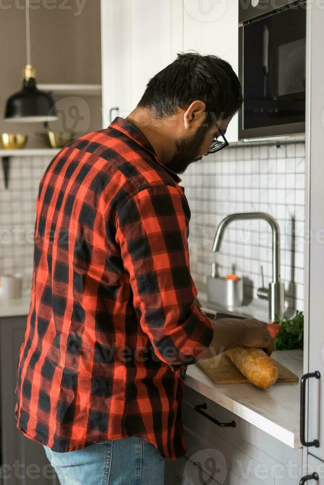 indiano ou latino homem cozinhando café da manhã enquanto em pé às a cozinha às lar, traseiro Visão foto