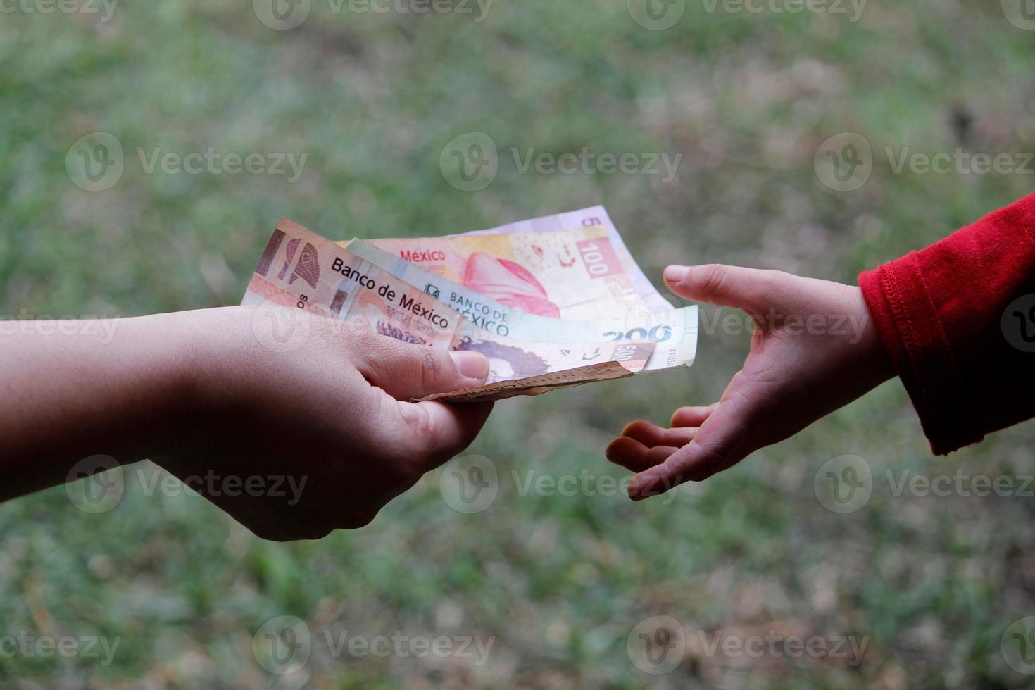 mão de uma mulher entregando dinheiro mexicano para a mão de um menor em um jardim foto