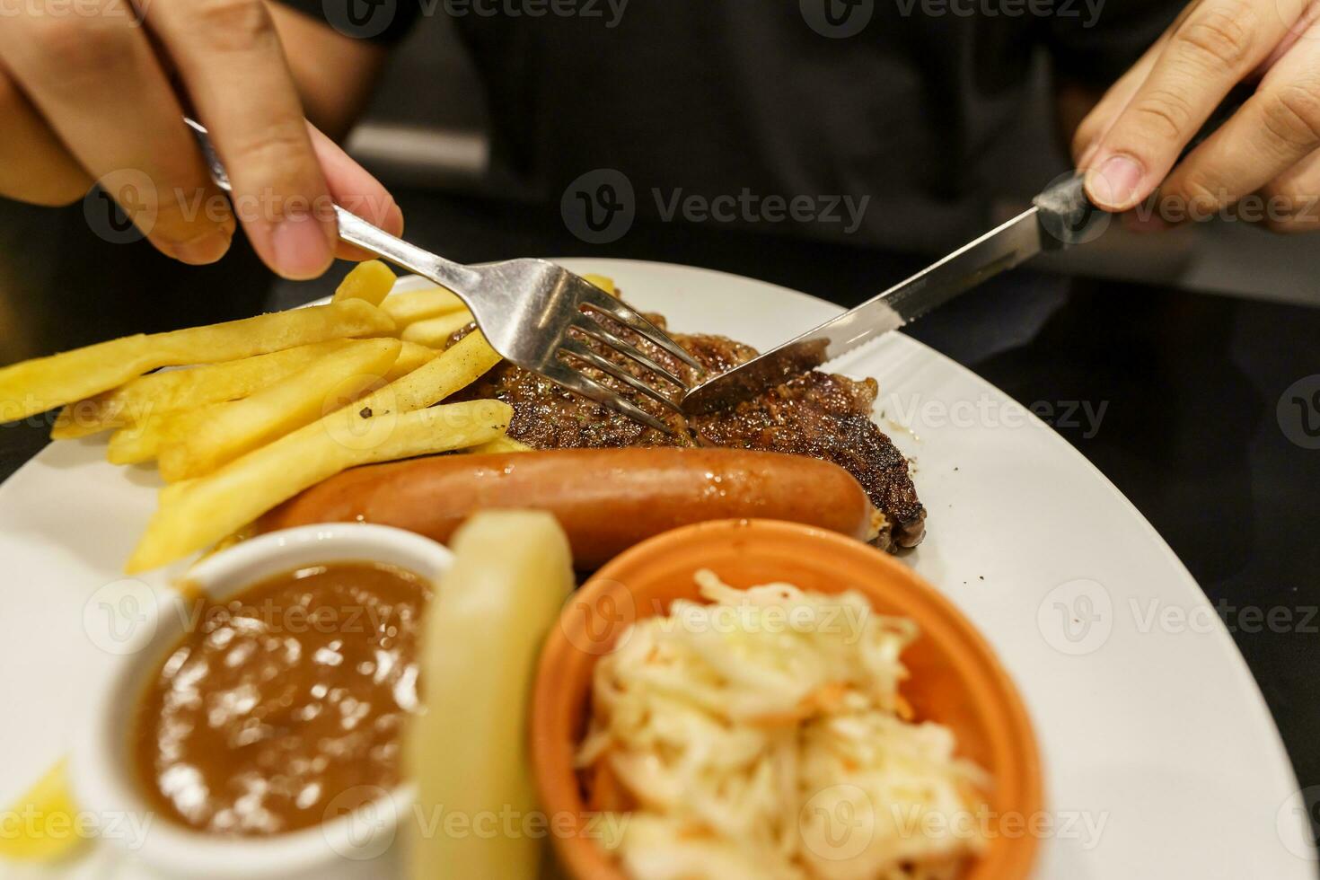 homem comendo grelhado carnes estaca a partir de placa. mão segurando faca e garfo corte grelhado carne bife foto