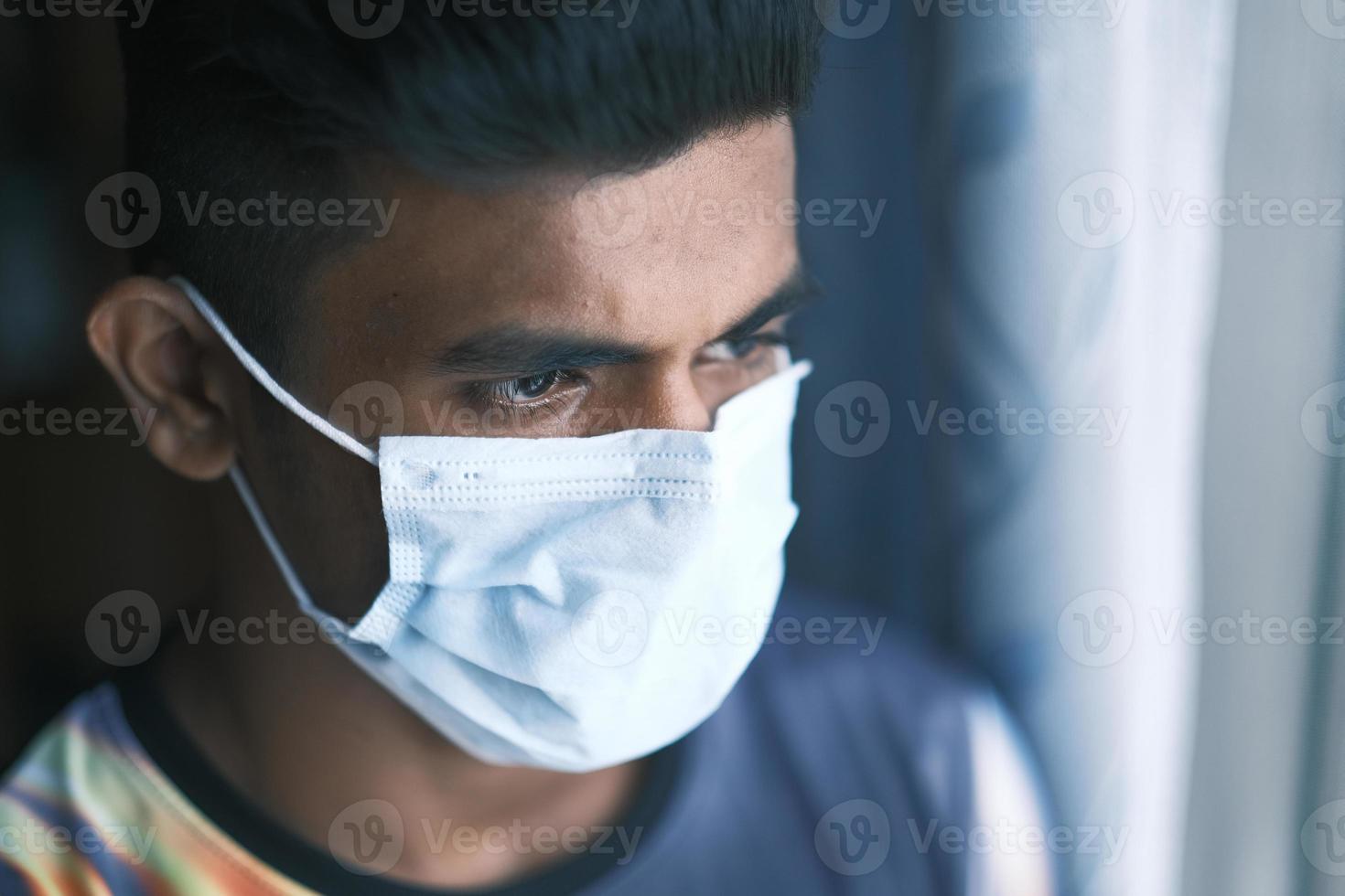um jovem com máscara protetora olhando pela janela foto