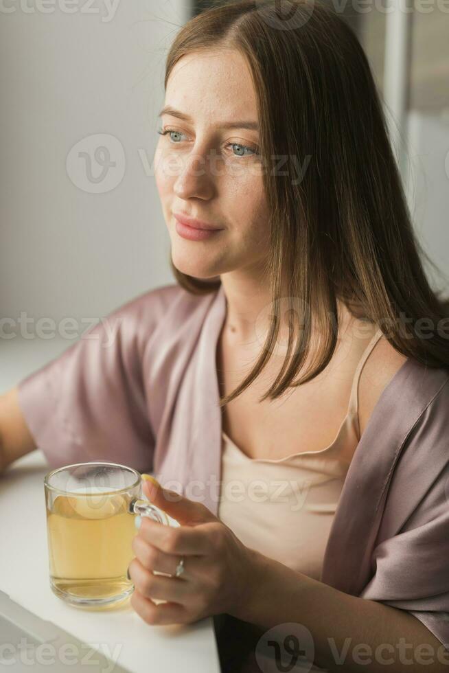 jovem mulher sentado em cadeira às casa e bebendo chá, casual estilo interior atirar. fechar-se retrato foto