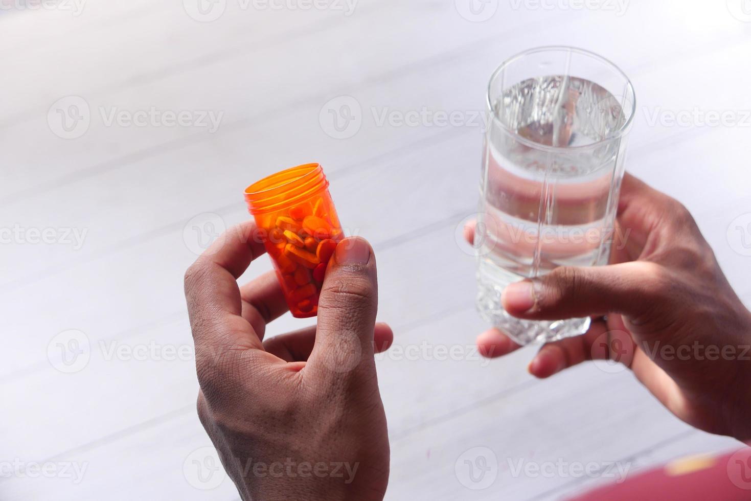 mão segurando o recipiente do comprimido e um copo d'água foto