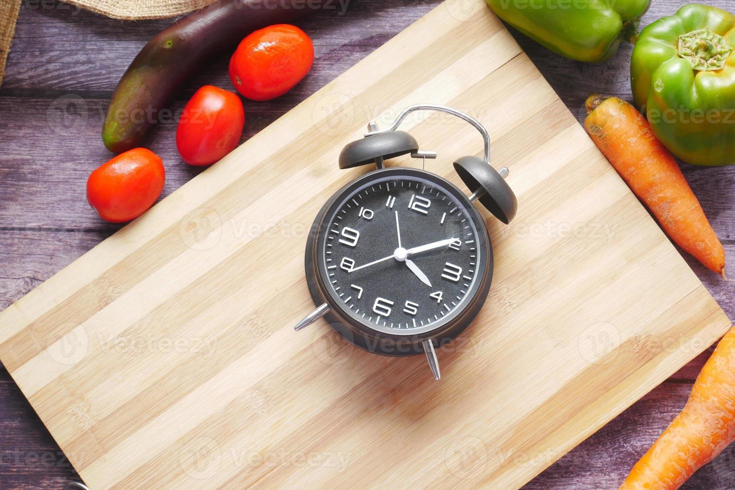 legumes frescos e despertador em uma tábua de cortar na mesa foto