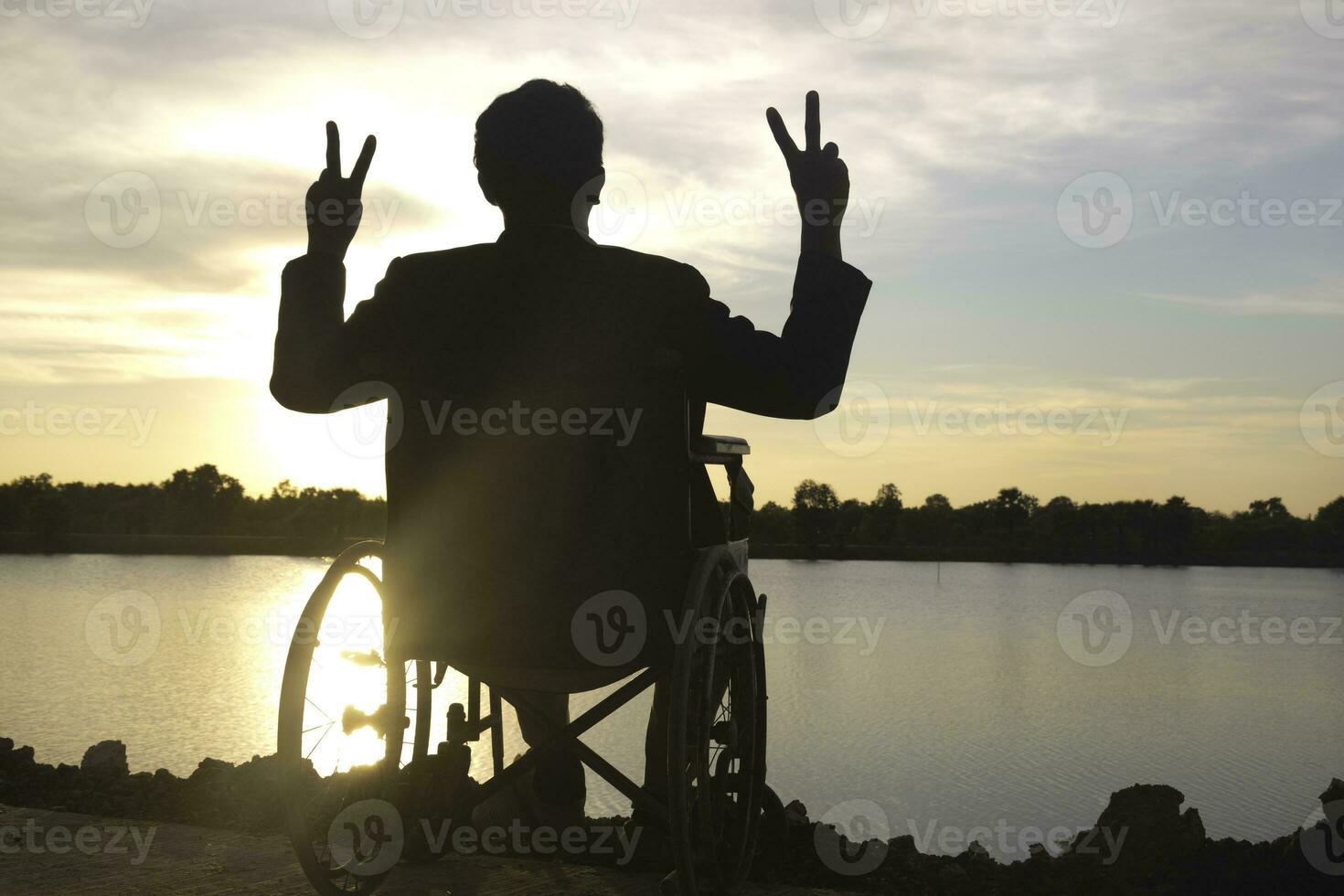 silhueta jovem Desativado homem vendo rio fundo.ele é levantar uma mão para e sentado em cadeira de rodas.desespero,solitário,esperança.foto conceito depressão e paciente. foto