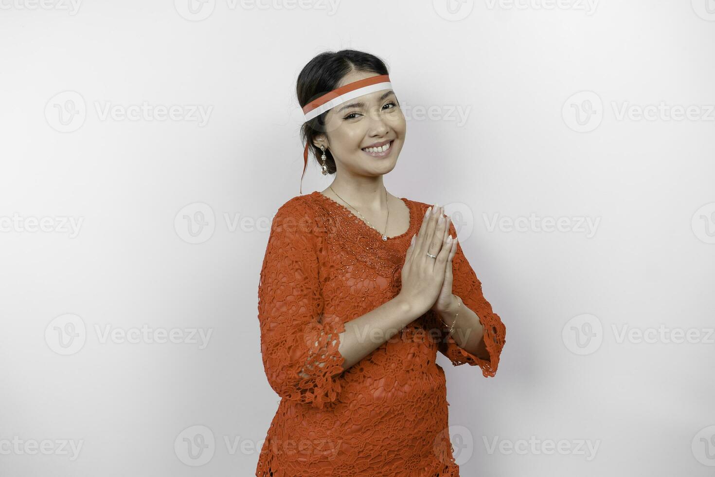 uma amigáveis indonésio mulher é vestindo vermelho kebaya gesticulando tradicional cumprimento e da indonésia bandeira arco de cabelo para comemoro Indonésia independência dia. isolado de branco fundo. foto