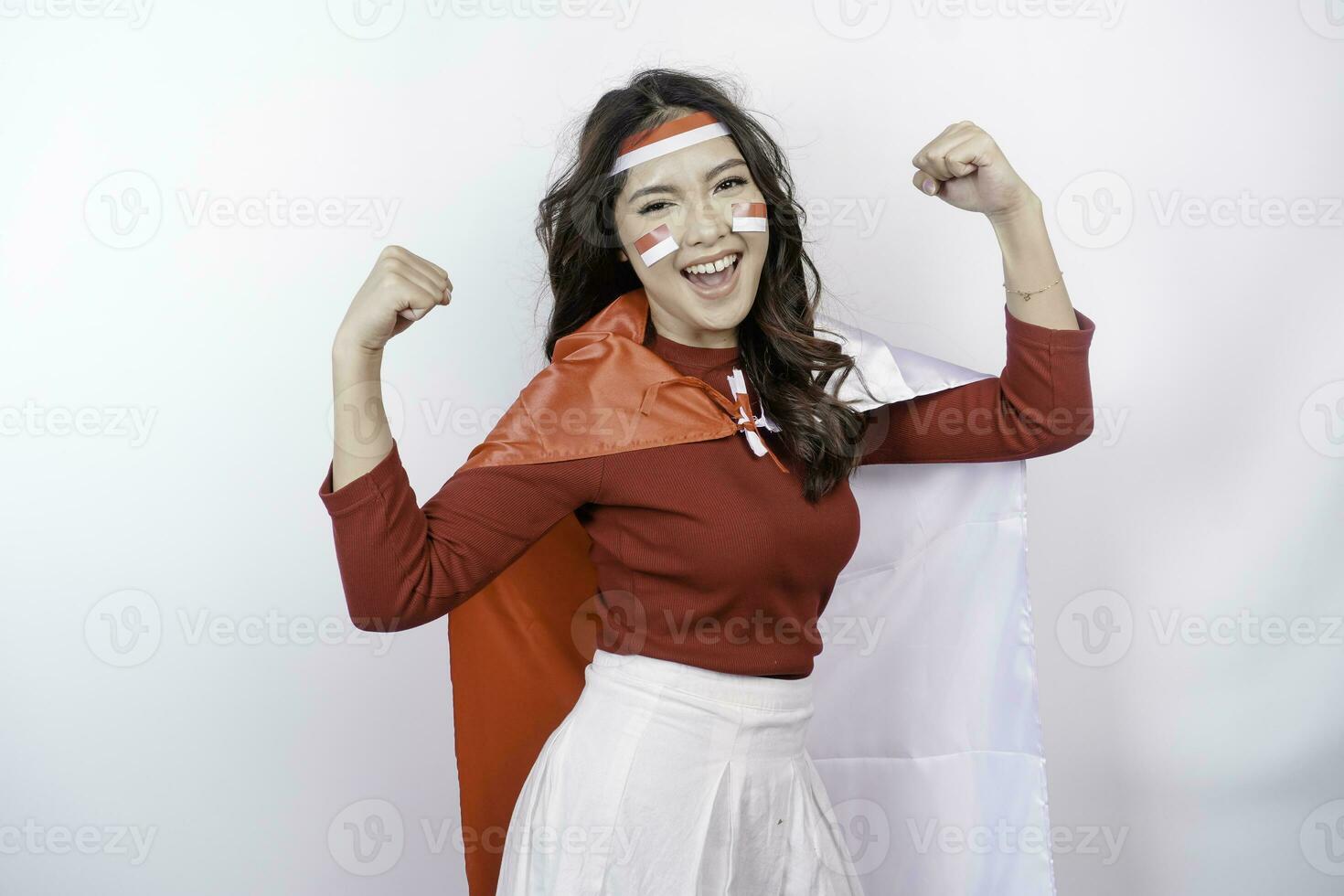 animado ásia mulher vestindo uma vermelho principal, bandeira capa e arco de cabelo, mostrando Forte gesto de elevação dela braços e músculos sorridente orgulhosamente. da indonésia independência dia conceito. foto