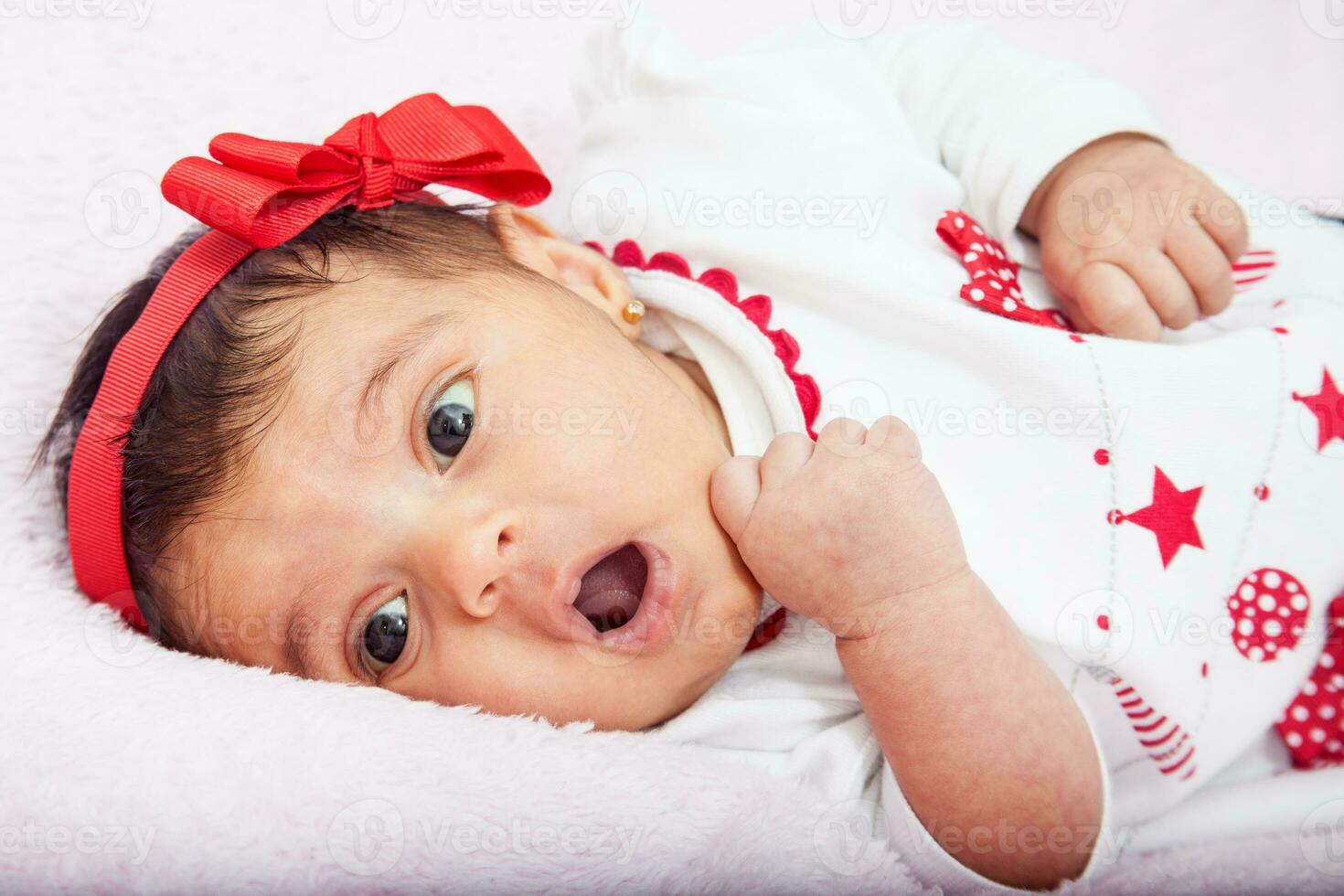 fechar-se do uma doce 1 mês bebê menina com uma surpresa expressão vestindo uma vermelho e branco t camisa. foto