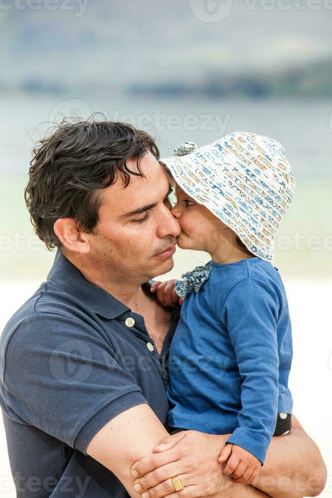doce bebê menina se beijando dela pai. jovem pai tendo Diversão com dele bebê menina às a lindo branco de praia do lago total localizado dentro a departamento do boyaca às 3.015 metros acima mar nível dentro Colômbia foto