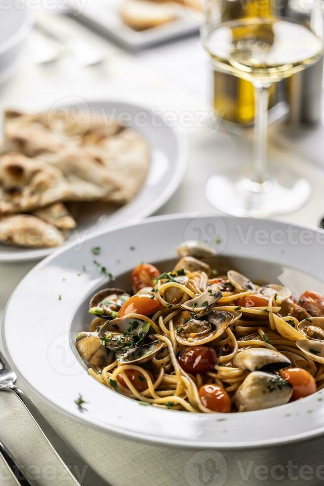 tradicional italiano espaguete alle vongole e pomodorini servido com pão sírio e branco vinho foto