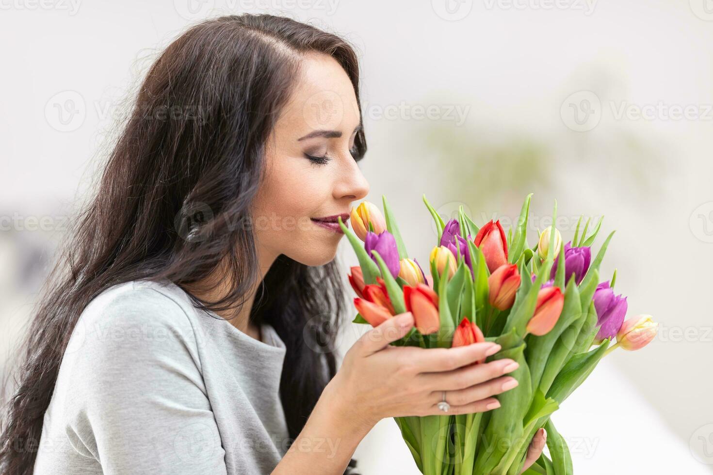 Sombrio cabelos mulher cheirando adorável aroma do fresco colorida tulipas foto