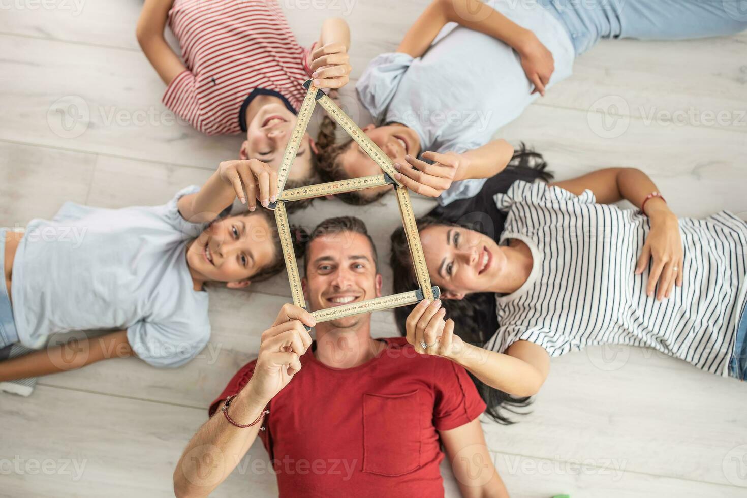 família deitado em seus costas em a chão aguarde juntos uma silhueta do uma casa fez Fora do de madeira dobrando metro foto