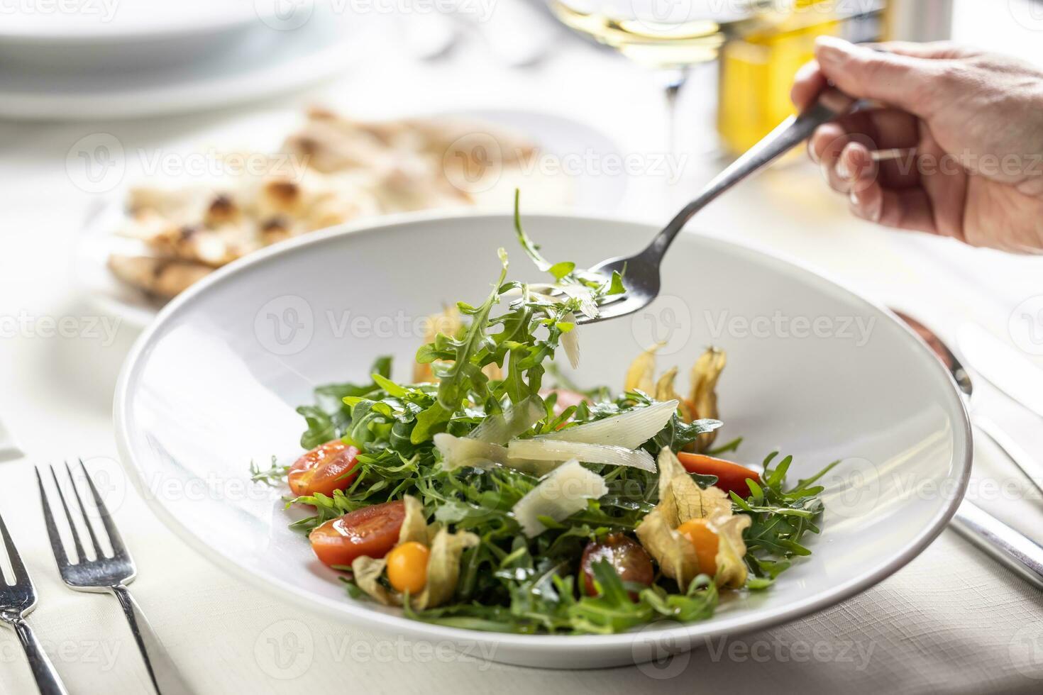 mão levando uma garfo com ruccola Fora do uma foguete salada dentro uma prato foto