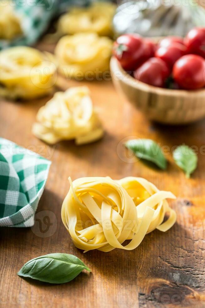 italiano massa tagliatelle em mesa com manjericão e tomates foto