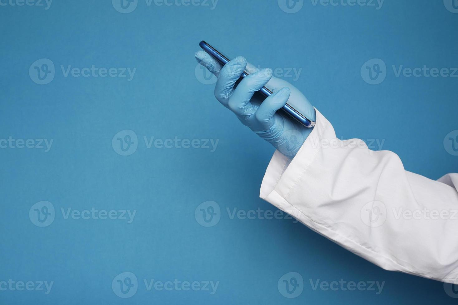mão do médico em luvas de proteção usando um smartphone contra um fundo azul foto