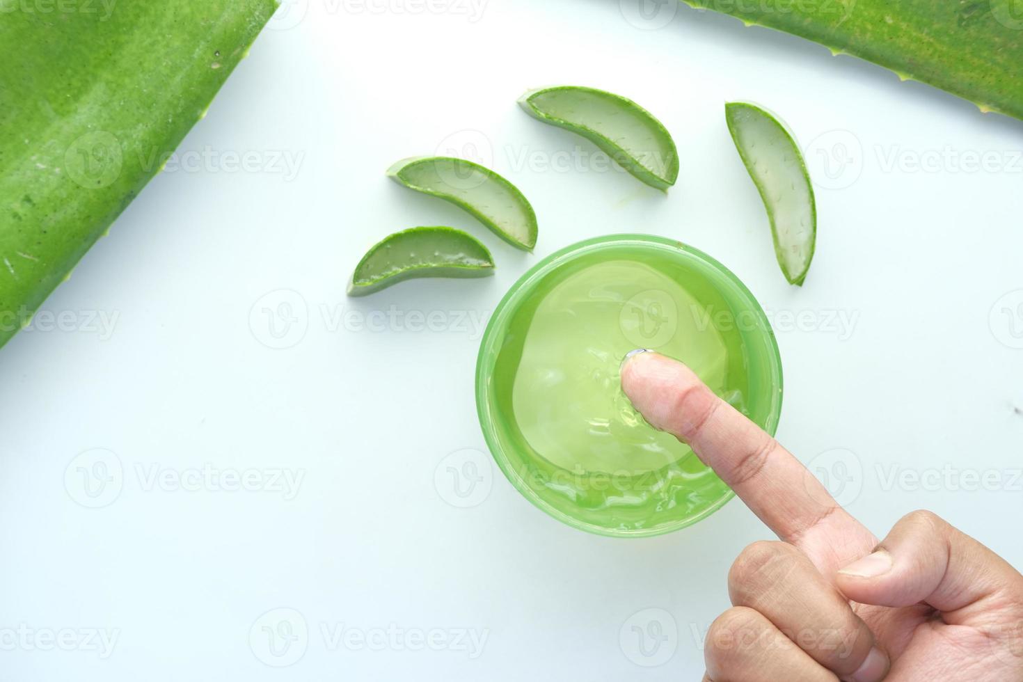 Aloe vera fresco fatiado e gel líquido em recipiente de plástico no fundo branco foto