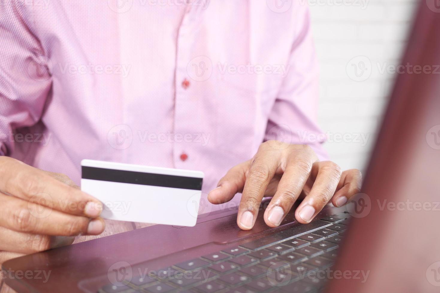 as mãos de um homem segurando um cartão de crédito e usando o laptop para fazer compras online foto