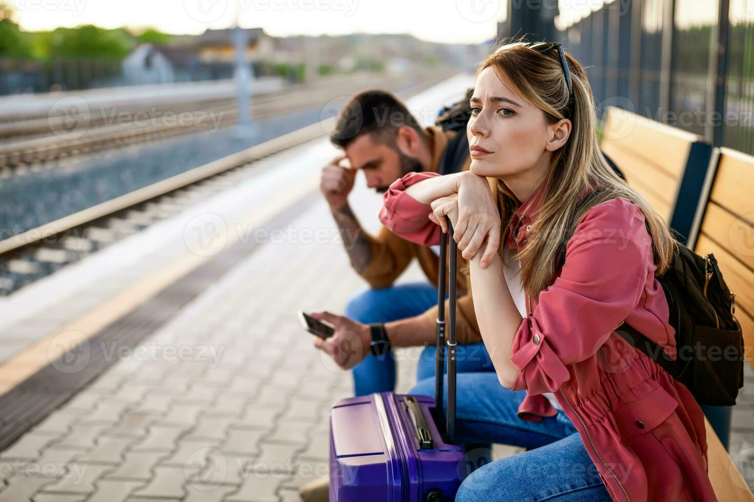 ansioso e cansado casal sentado às estrada de ferro estação e esperando para chegada do seus trem. foto