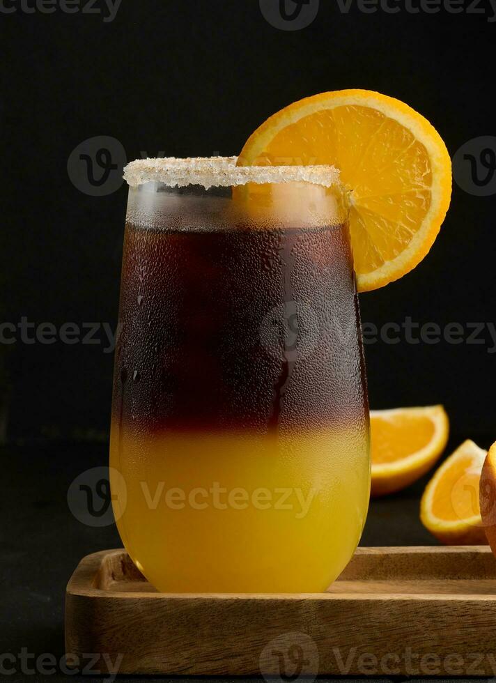 gelado café com laranja suco dentro uma transparente vidro, refrescante bumble café em a mesa, Preto fundo foto