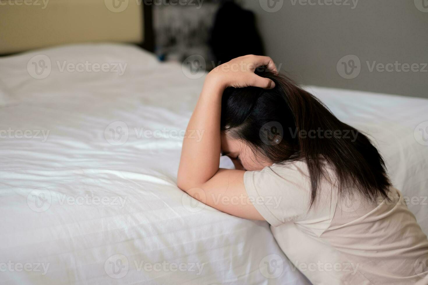 triste depressivo Ásia mulher sofrimento em a branco cama, ela é sentado dentro cama e tocante dela testa, dormir transtorno e estresse conceito foto