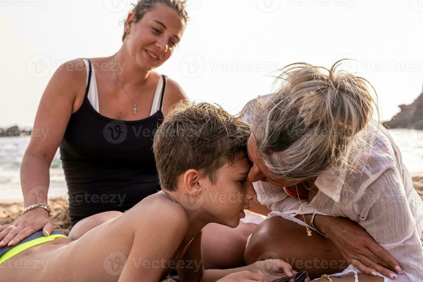 lindo meio envelhecido mãe com dela dois filhos relaxante em a de praia às pôr do sol foto