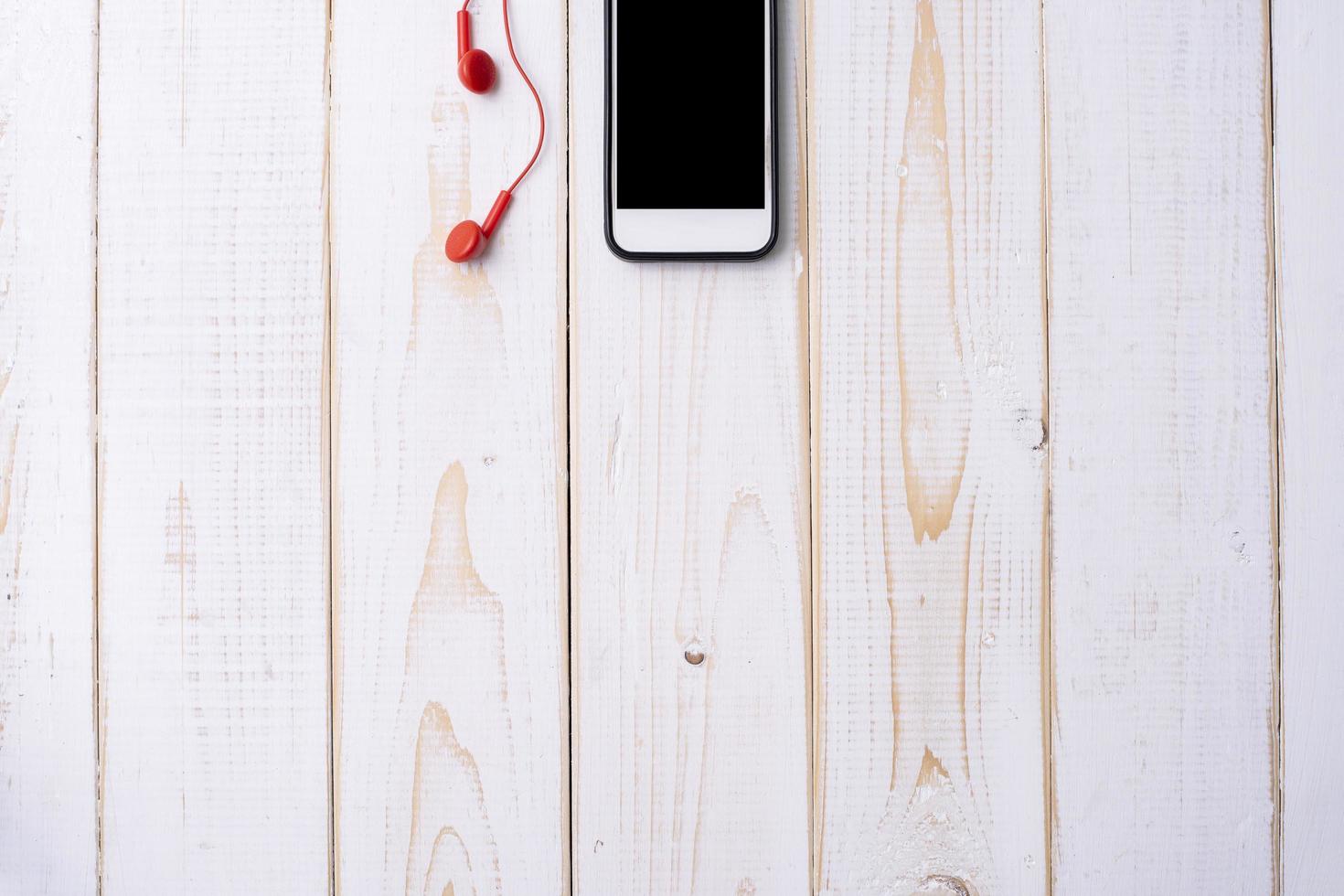 Smartphone e fone de ouvido vermelho na mesa de madeira branca foto