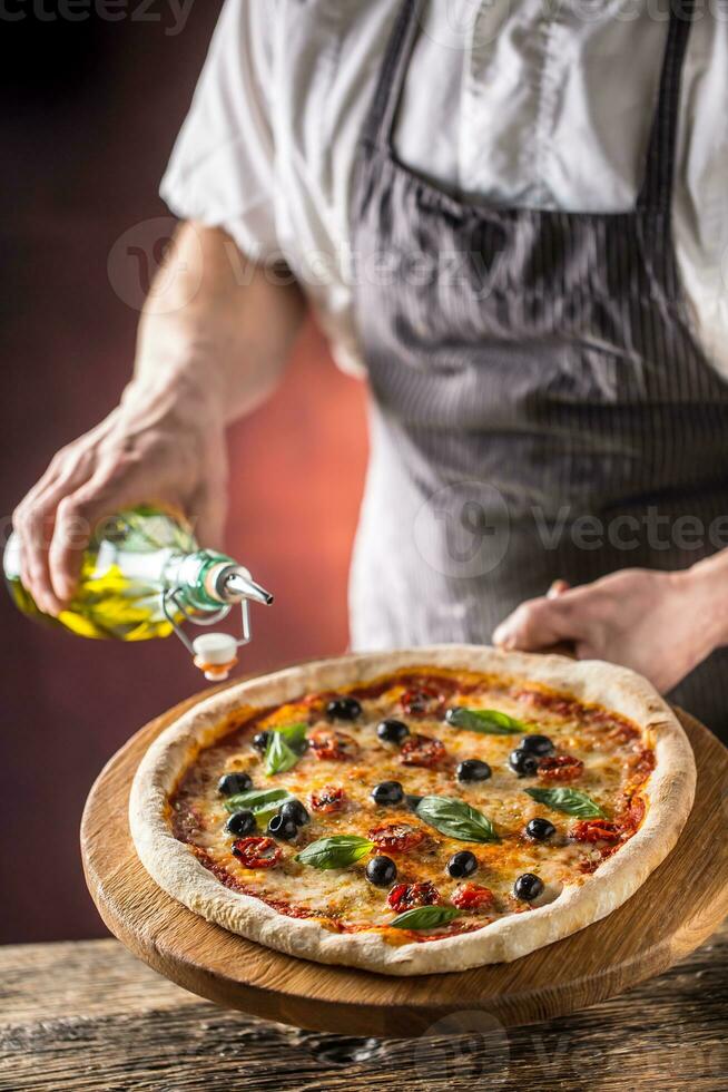 chefe de cozinha e pizza. chefe de cozinha derramando Oliva óleo em pizza dentro hotel ou restaurante foto