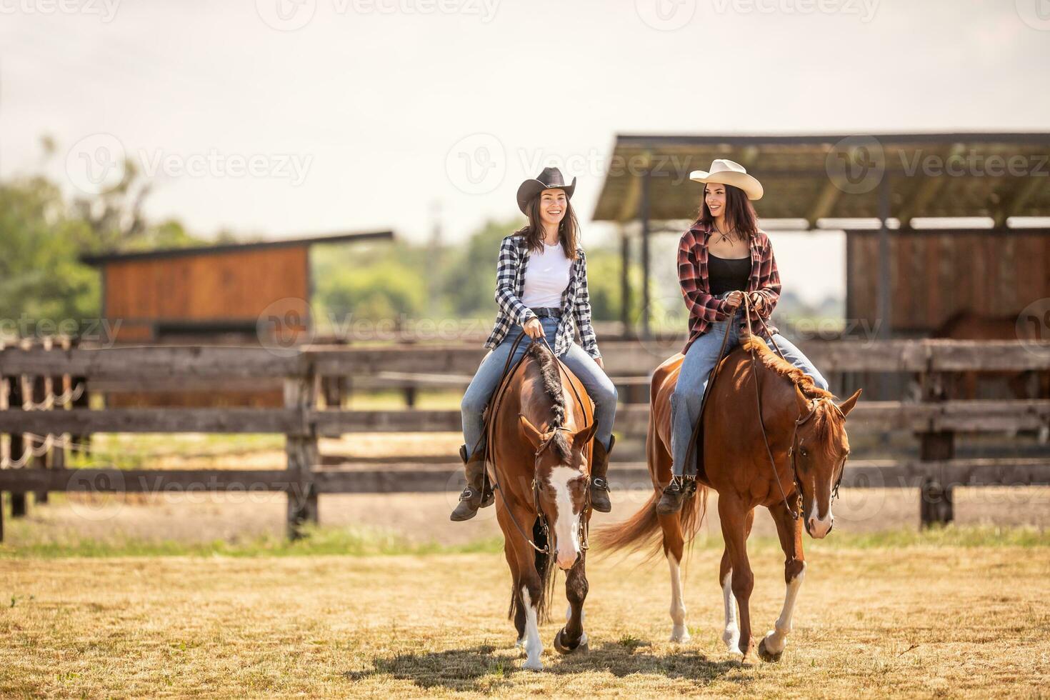 dois vaqueiras equitação seus cavalos em uma rancho durante quente verão dia foto