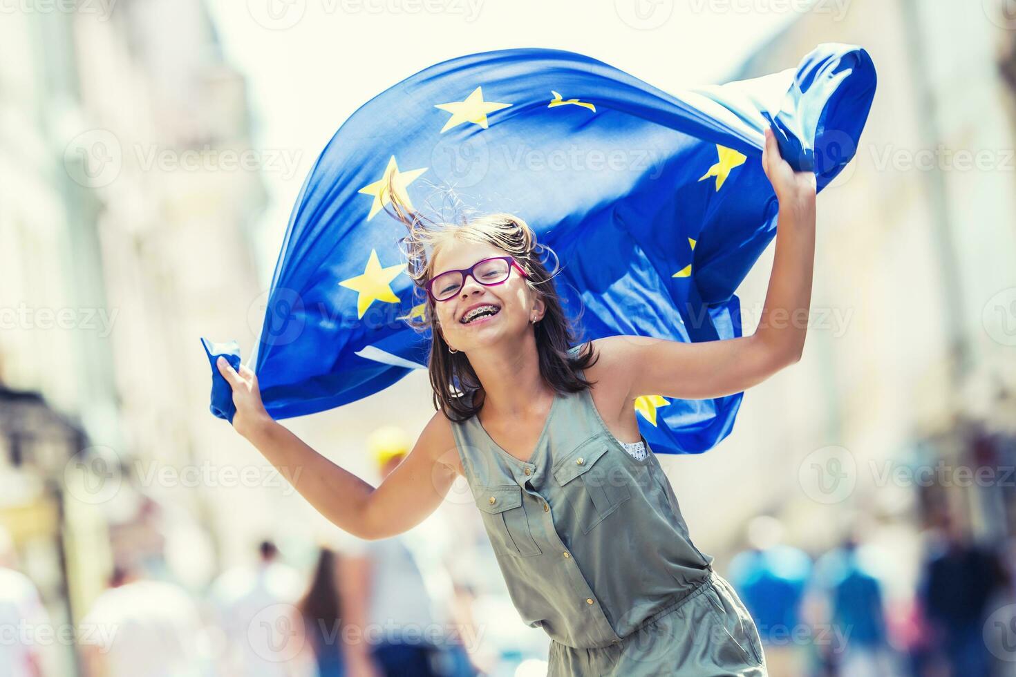 eu bandeira. fofa feliz menina com a bandeira do a europeu União. jovem Adolescência menina acenando com a europeu União bandeira dentro a cidade foto