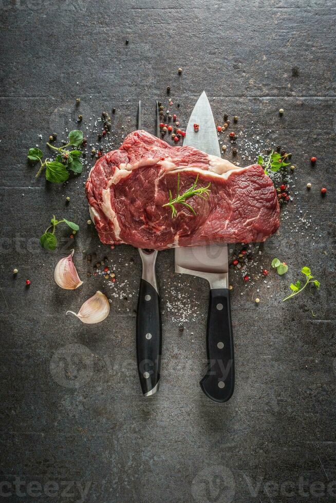 cru carne bife com garfo e faca sal Pimenta e ervas em Sombrio concreto fundo foto