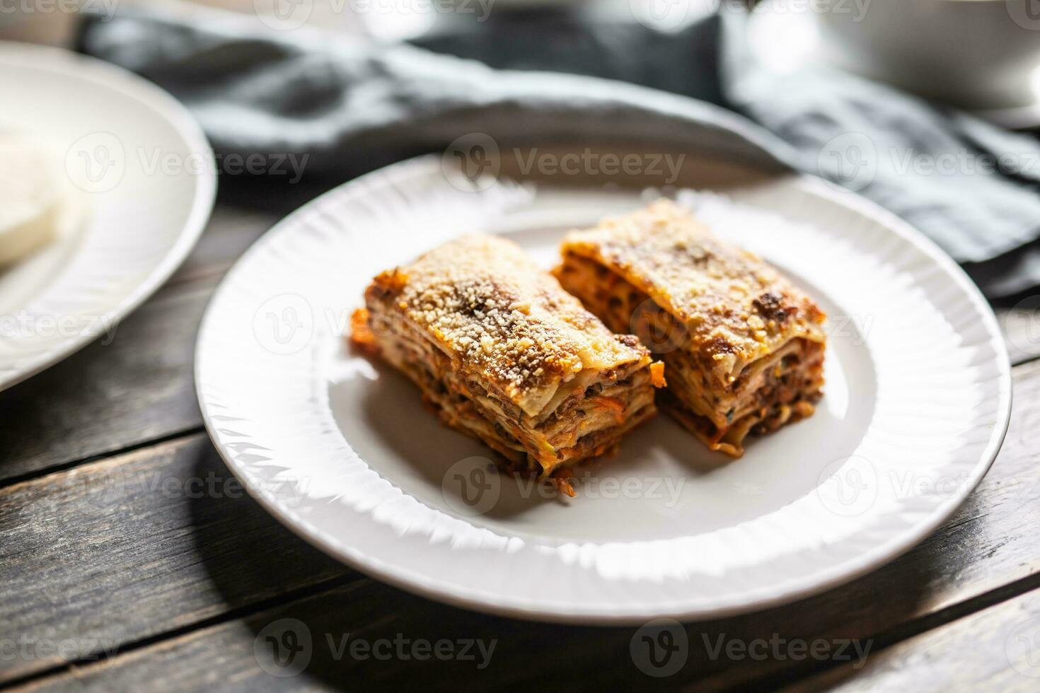 dois peças do lasanha servido em uma branco prato coberto com Grato parmesão queijo foto