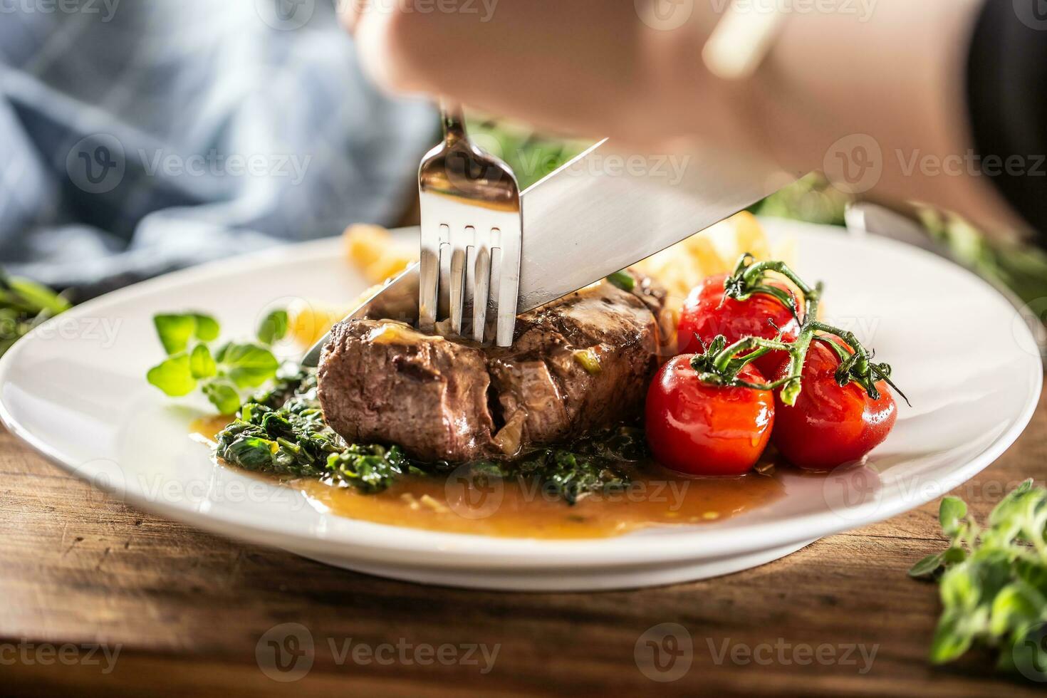 pessoa cortes para dentro uma cozinhou bife com garfo e faca com legumes em uma lado foto